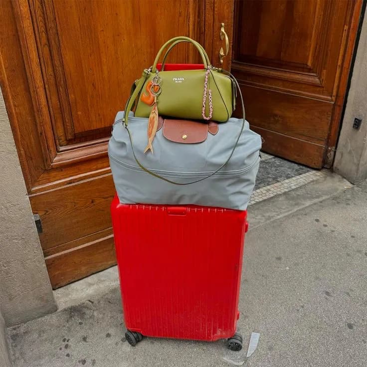 A red carry-on suitcase with two bags stacked on top, waiting outside an old wooden door