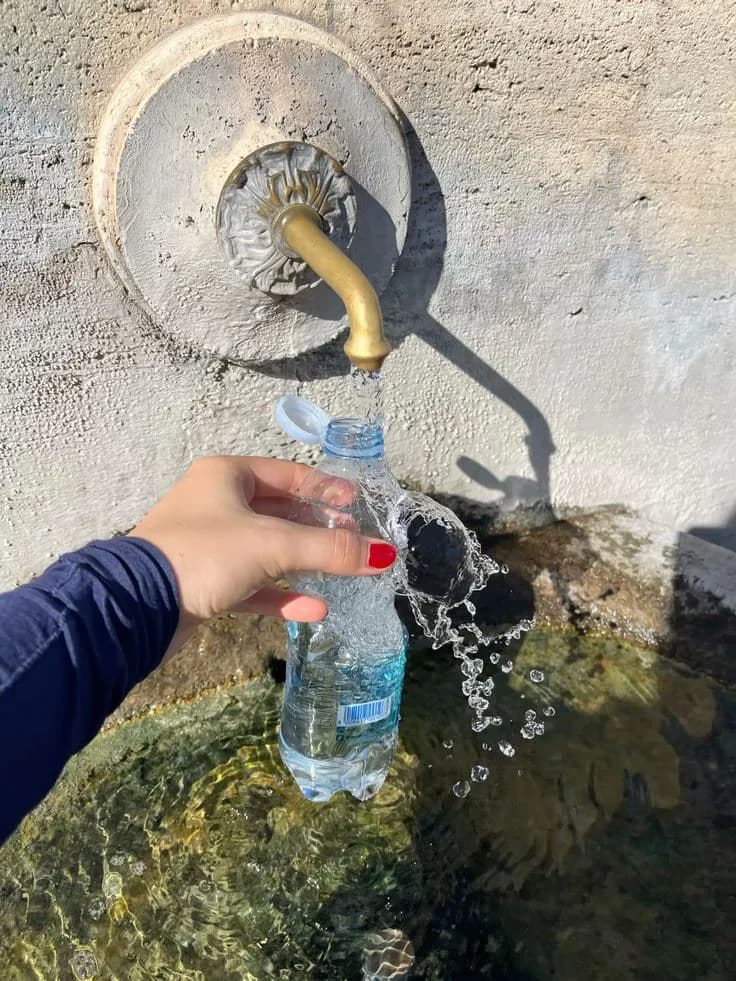 Refilling a plastic bottle at a stone drinking fountain in Rome